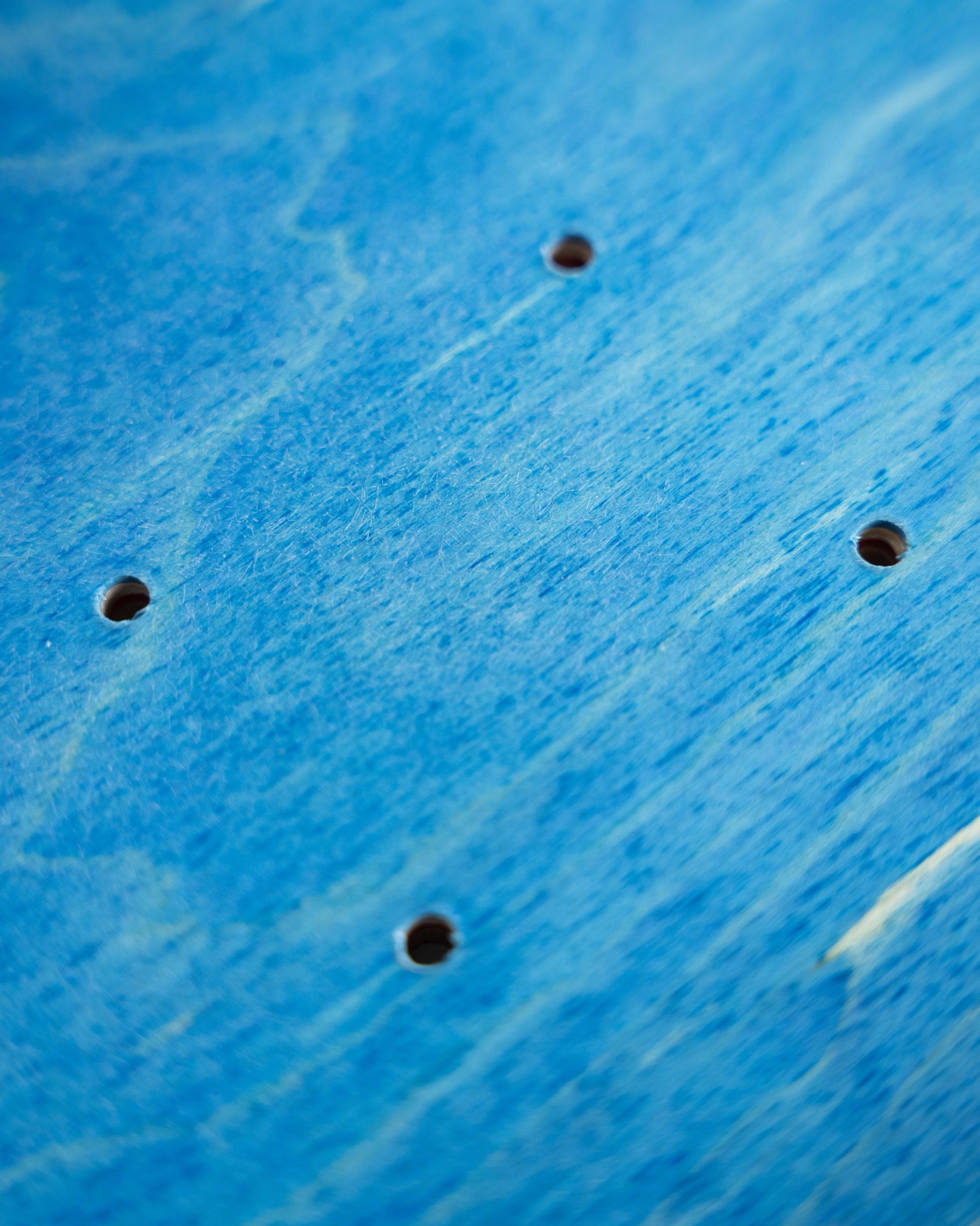 Close-up of a bright blue textured surface with four evenly spaced circular holes, likely part of a product detail shot.